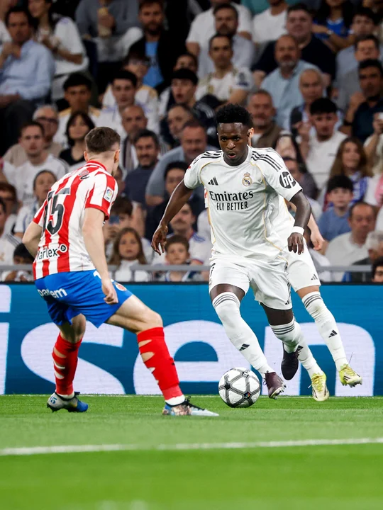 "Plano medio de Vinícius Jr. encarando con intensidad a un jugador rival del Girona en un partido de LaLiga. Se observa la postura competitiva del brasileño intentando el regate en la banda durante el encuentro de abril de 2026."